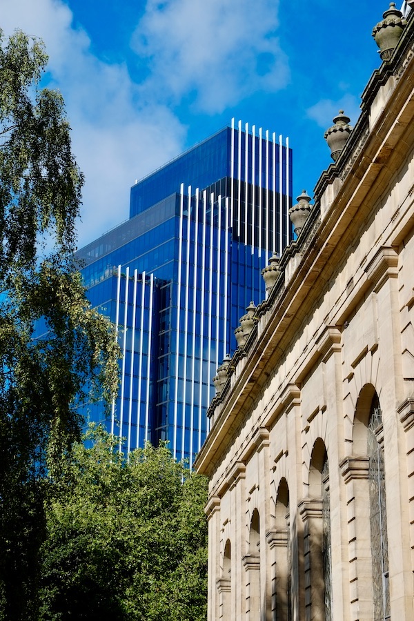 The side wall of a cathedral is visible on the right, with trees and a skyscraper in the background