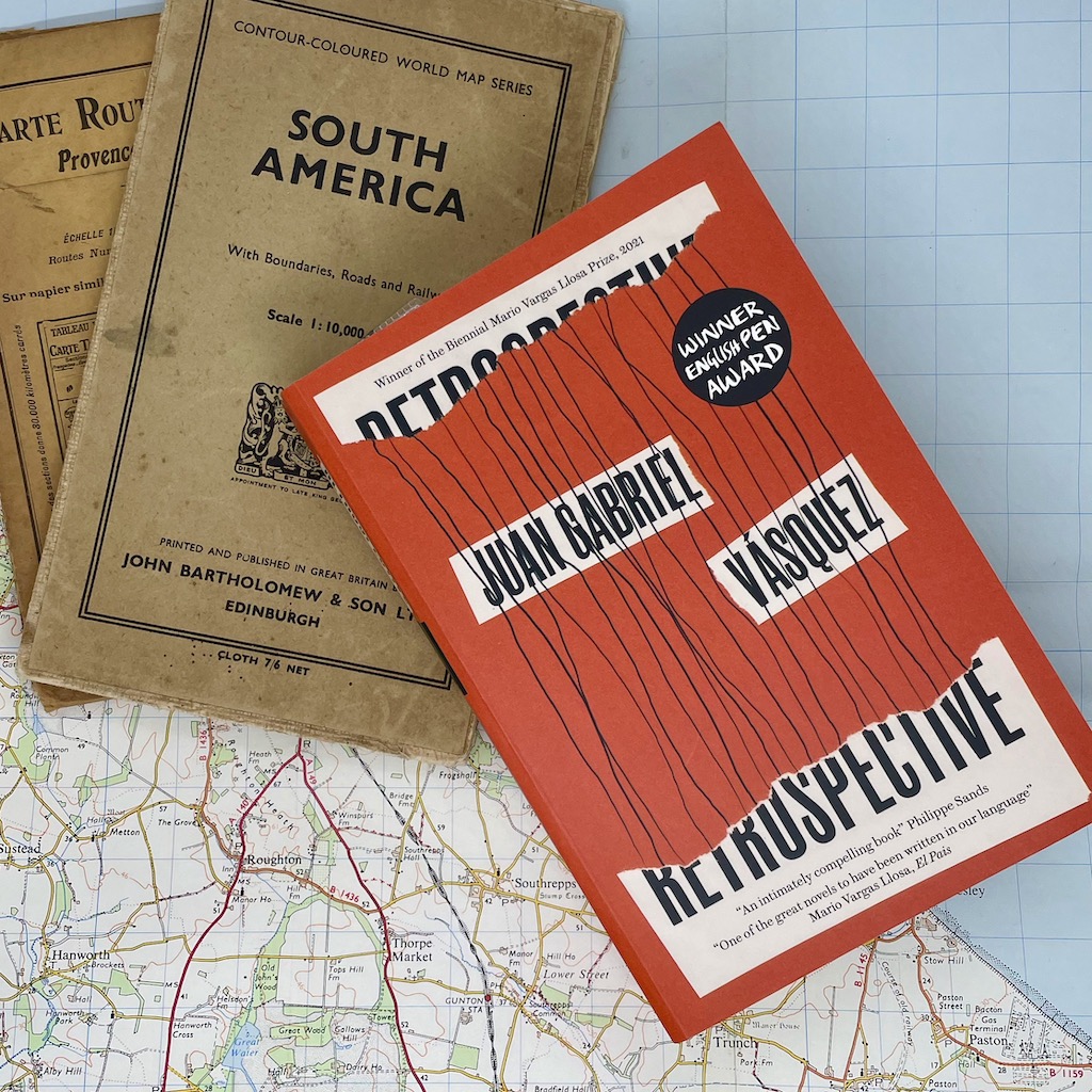 A book with a red cover sits on top of a map, with a couple of old folded maps of South America underneath.