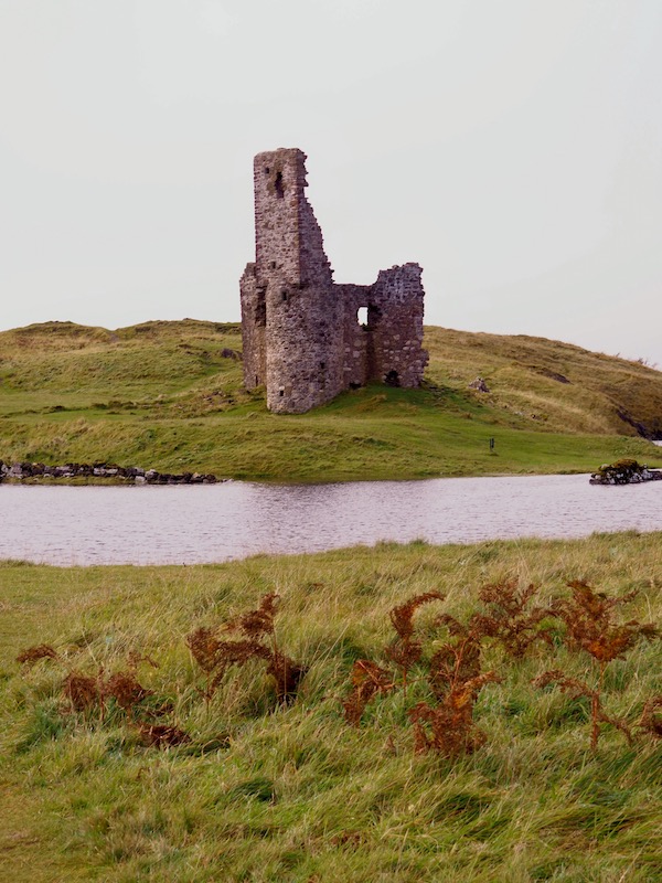 A ruined stone castle stands on an island surrounded by water.