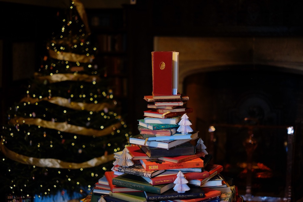 A Christmas tree made of books with a real tree behind