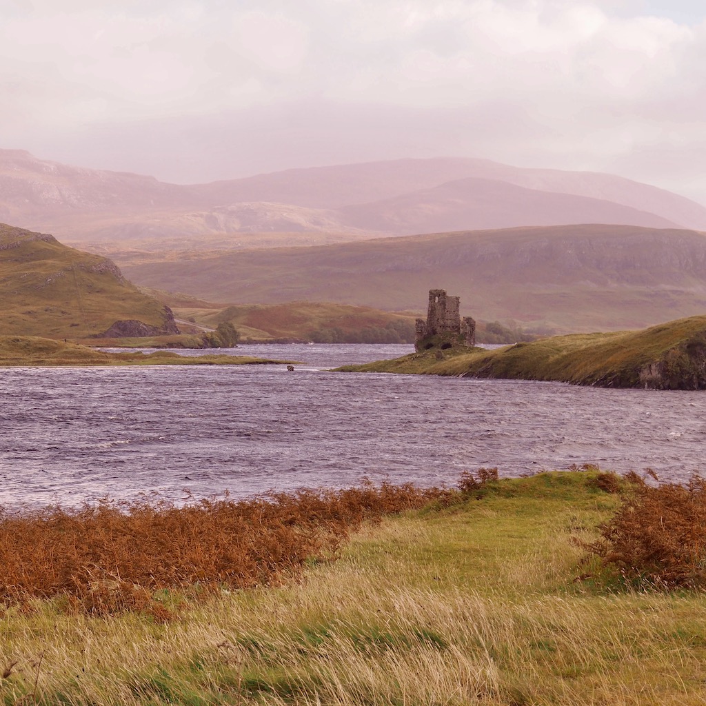 A loch with a castle at it's side. There are hills in the background