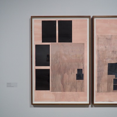 Two pink landscape artworks. Each has black squares on them. They represent images stuck around the mirror in a barbers shop.