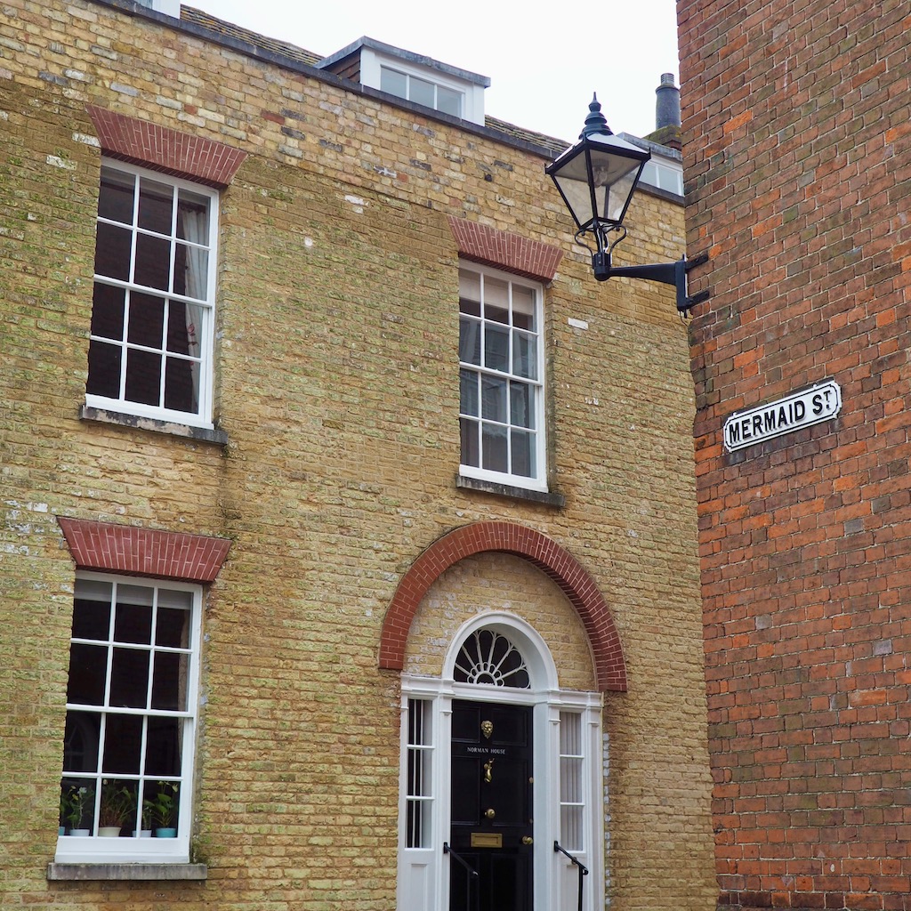 A colour photo of two georgian houses on a street corner. One is red brick and the other is yellow. There is a streetlamp and a sign saying Mermaid Street