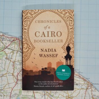 A colour photo of Chronicles of a Cairo Bookseller, by Egyptian author, Nadia Wassef. The cover is peach and shows a city skyline. The book lies on a map.
