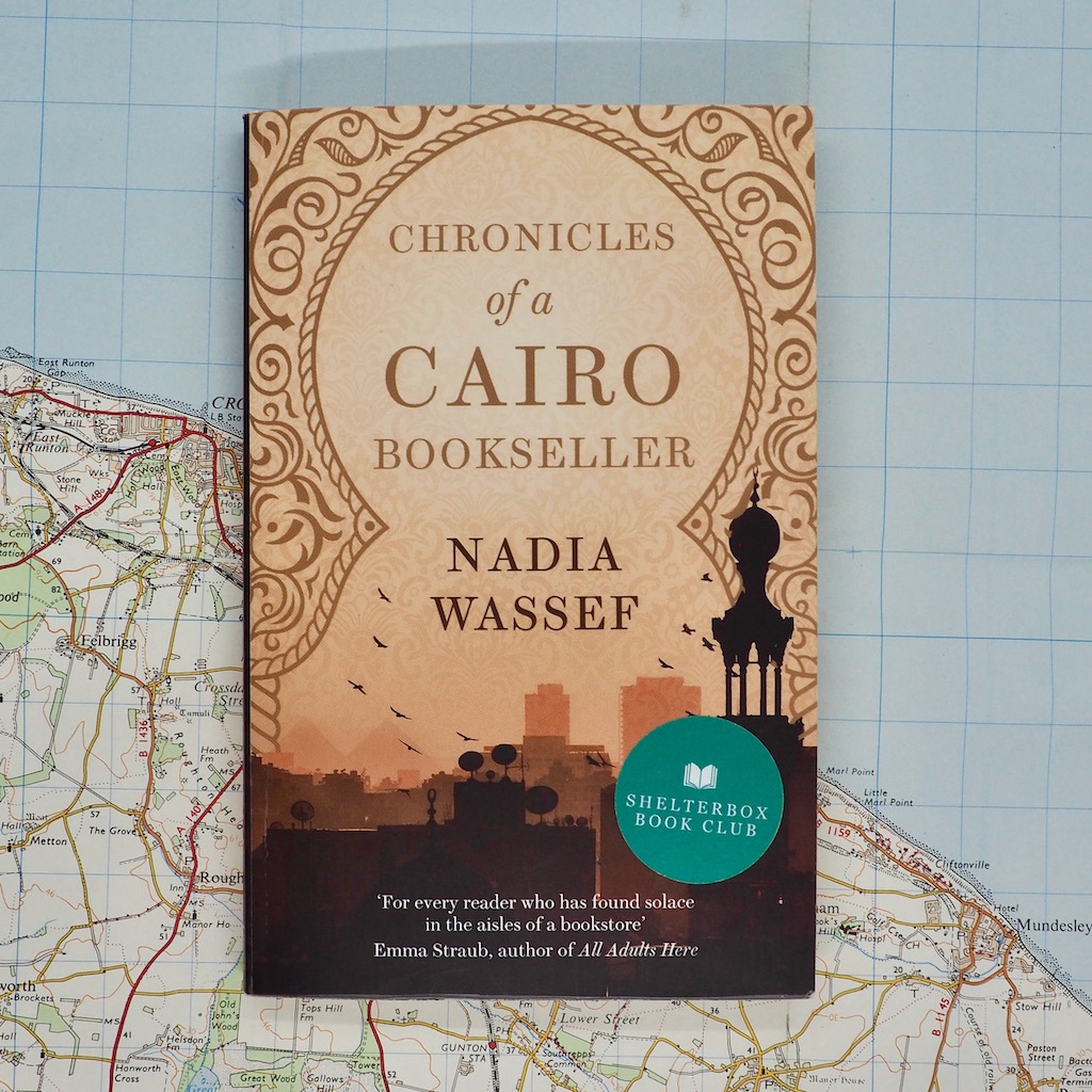 A colour photo of Chronicles of a Cairo Bookseller, by Egyptian author, Nadia Wassef. The cover is peach and shows a city skyline. The book lies on a map.
